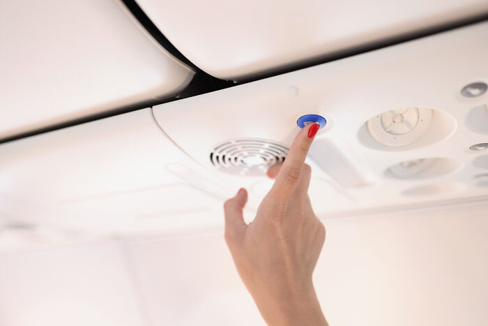 Passenger pressing a call button in an airplane cabin, highlighting common passenger habits annoying flight attendants. Passenger pressing a call button in an airplane cabin, highlighting common passenger habits annoying flight attendants.