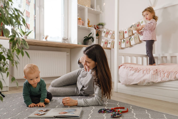 18-year-old woman caring for two kids in a bright room, playing with them while lying on a carpeted floor. 18-year-old woman caring for two kids in a bright room, playing with them while lying on a carpeted floor.