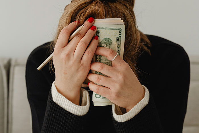 Woman covering face with hands and cash, illustrating internet debates on whether paying for hen parties is excessive. Woman covering face with hands and cash, illustrating internet debates on whether paying for hen parties is excessive.