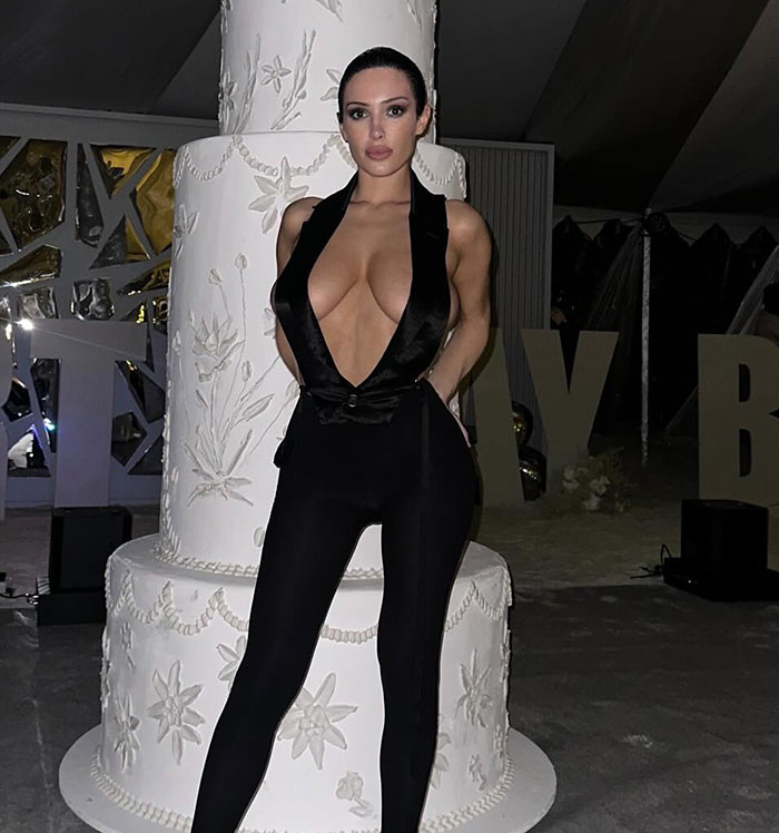 Bianca Censori posing in a revealing black outfit with a deep neckline at a nighttime event setting. Bianca Censori posing in a revealing black outfit with a deep neckline at a nighttime event setting.
