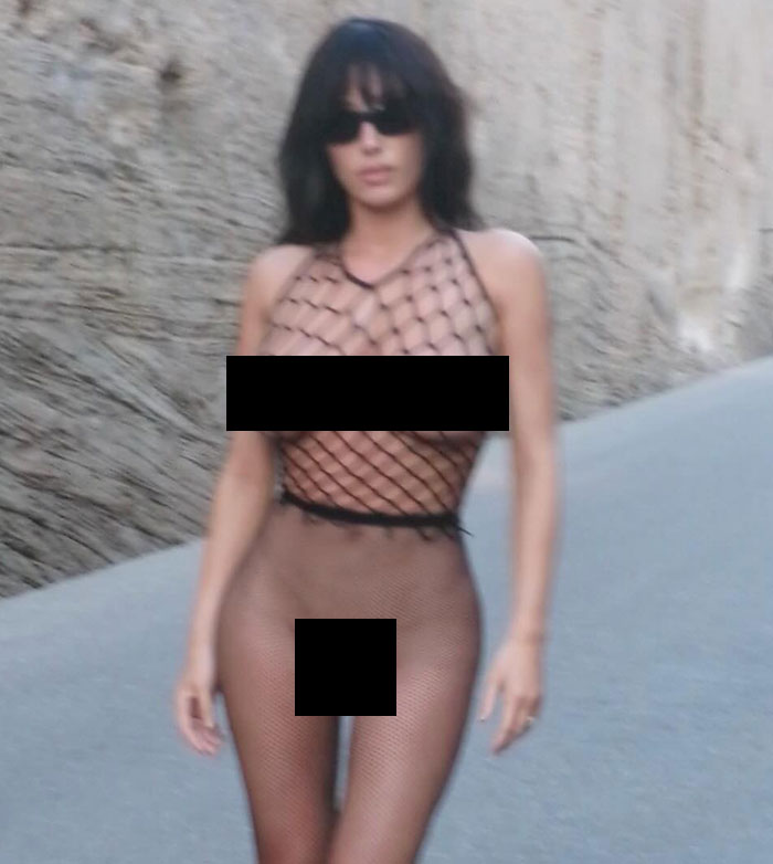 Bianca Censori wearing revealing fishnet outfit and sunglasses while walking outdoors on a gray paved path. Bianca Censori wearing revealing fishnet outfit and sunglasses while walking outdoors on a gray paved path.