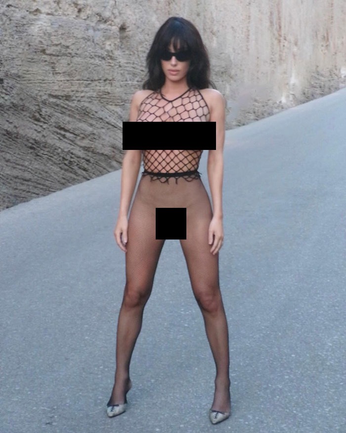 Bianca Censori posing outdoors in revealing fishnet outfit with sunglasses, sparking public calls for arrest over indecency. Bianca Censori posing outdoors in revealing fishnet outfit with sunglasses, sparking public calls for arrest over indecency.