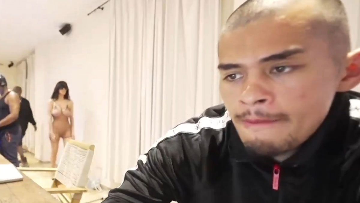 A man quickly covering the camera while Bianca Censori walks in barely dressed in a room with curtains.