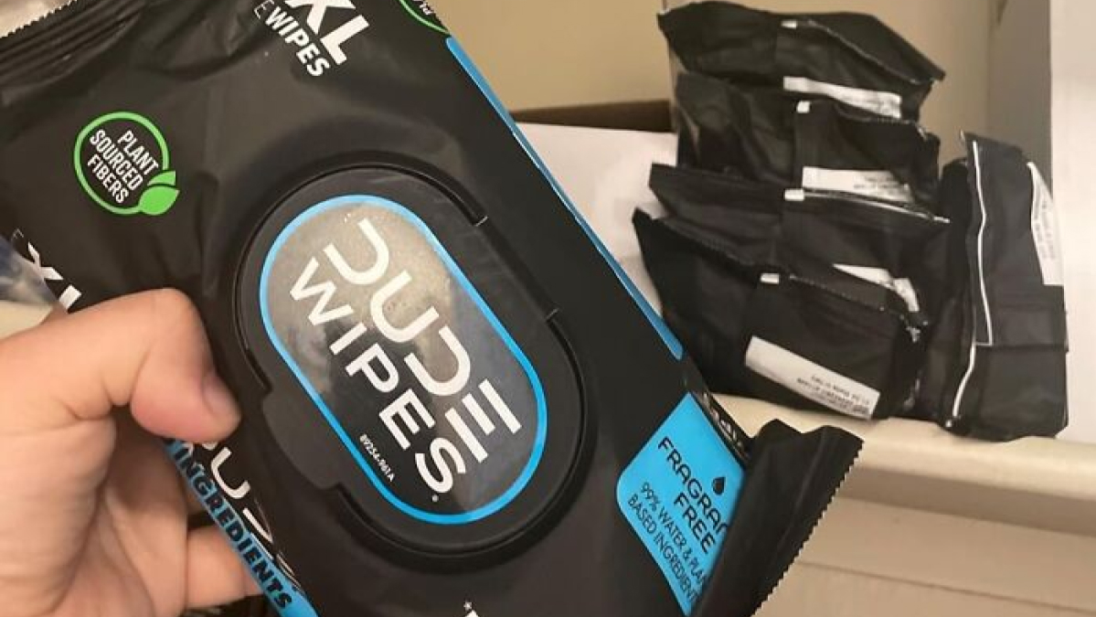 Hand holding Dude Wipes package, one of the biggest Shark Tank success stories, with more packs in background.