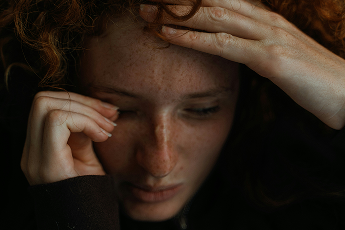 Stressed woman with red hair and freckles holding her head, representing emotional support during a family member's military service. Stressed woman with red hair and freckles holding her head, representing emotional support during a family member's military service.
