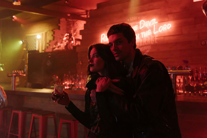 Couple in dimly lit bar, man hugging woman while she holds a drink, reflecting tension in an open relationship setting. Couple in dimly lit bar, man hugging woman while she holds a drink, reflecting tension in an open relationship setting.