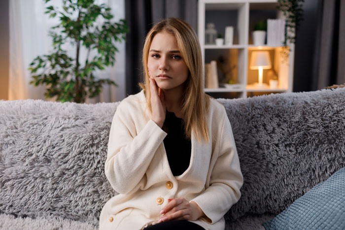 Young woman looking frustrated on couch, reflecting on helicopter parents treating son’s girlfriend like a nanny. Young woman looking frustrated on couch, reflecting on helicopter parents treating son’s girlfriend like a nanny.