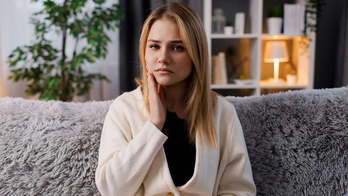 Young woman sitting on couch looking frustrated, representing helicopter parents treating sonu2019s girlfriend like nanny and planner.