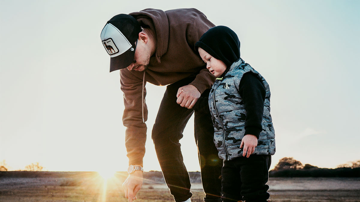 Man watching child outdoors during sunset, reflecting on experience of trip with girlfriendu2019s family and kids care.