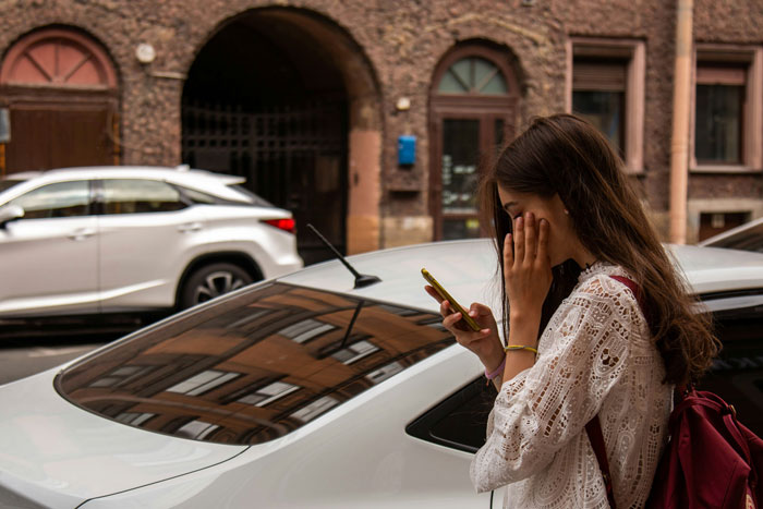 Young woman outside near cars, looking upset while checking her phone, relating to song performance connection conflict. Young woman outside near cars, looking upset while checking her phone, relating to song performance connection conflict.