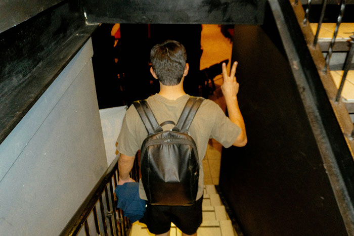 Young guy with backpack walking down stairs, making a peace sign, showing displeasure with girlfriend's school song performance connection. Young guy with backpack walking down stairs, making a peace sign, showing displeasure with girlfriend's school song performance connection.