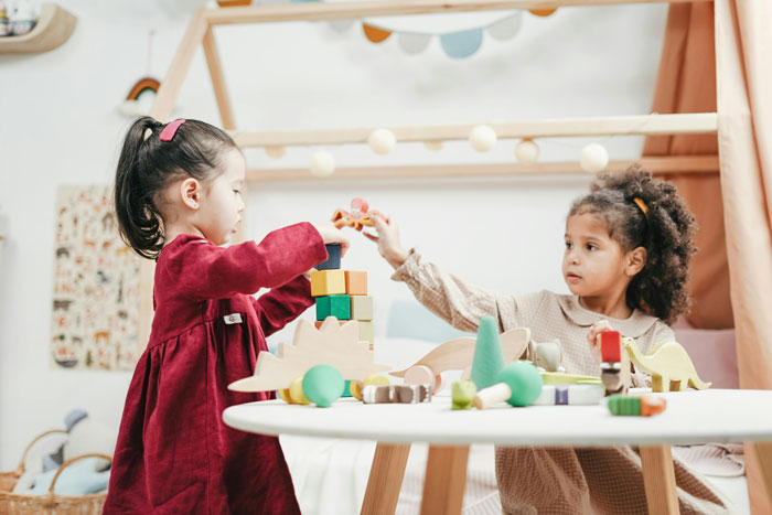 Two children playing with toys at a table while parents invite couple on vacation for free babysitting. Two children playing with toys at a table while parents invite couple on vacation for free babysitting.