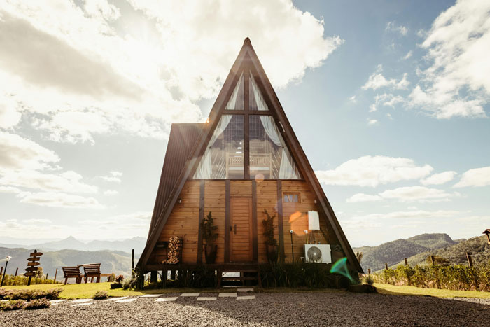 A-frame vacation cabin in sunlight with mountains in background symbolizing parents inviting couple for free babysitting. A-frame vacation cabin in sunlight with mountains in background symbolizing parents inviting couple for free babysitting.
