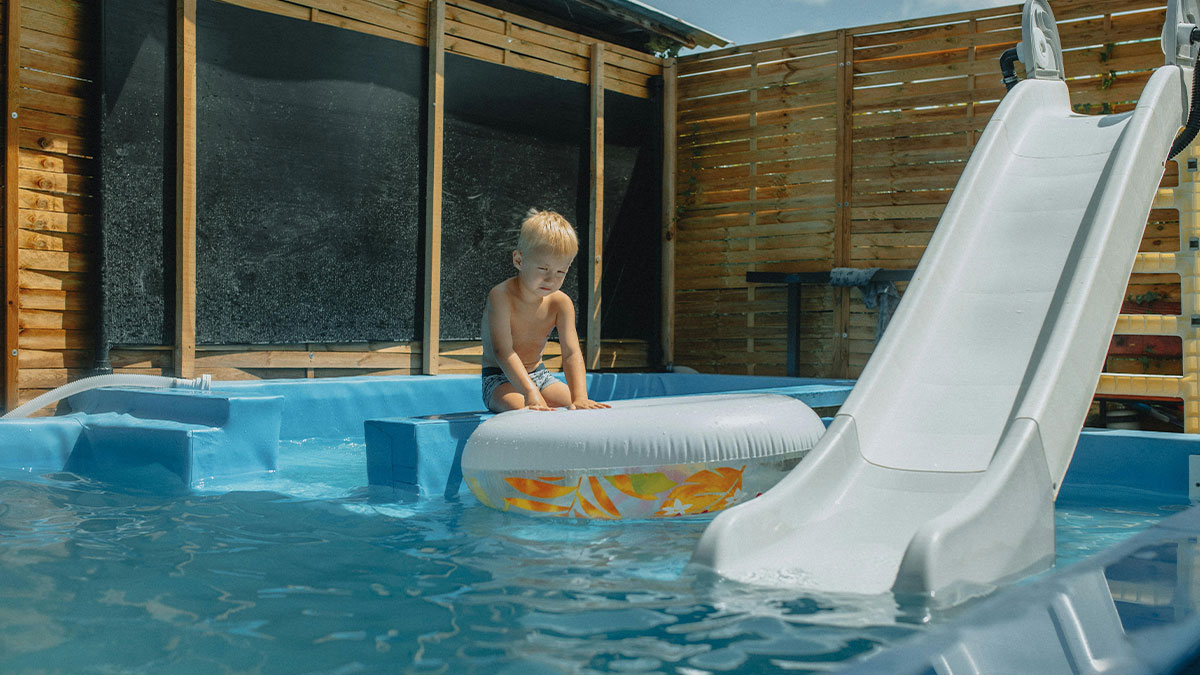 Young boy sitting on a pool float in a backyard pool near a slide, illustrating lifeguard rescue and drowning safety.