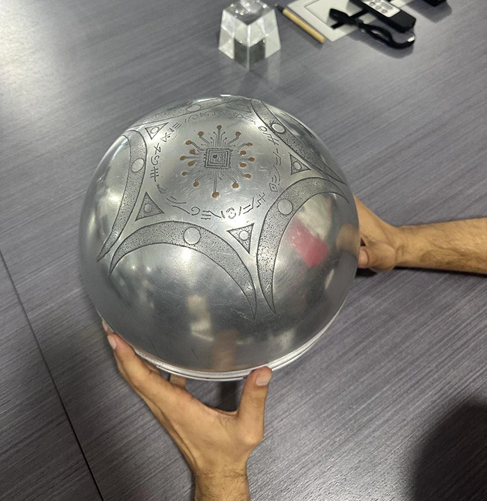 Metallic UFO with ominous symbols and writing about origin of birth, held by hands on a gray wooden table surface. Metallic UFO with ominous symbols and writing about origin of birth, held by hands on a gray wooden table surface.