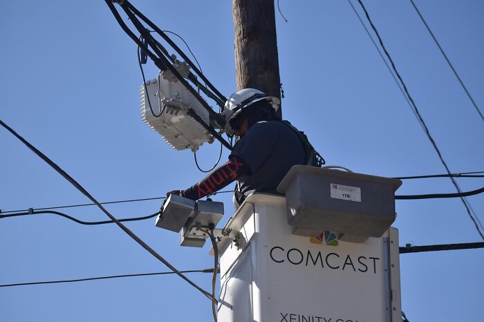 Utility worker repairing electrical or communication lines from a Comcast bucket truck, people share companies bad list concept.