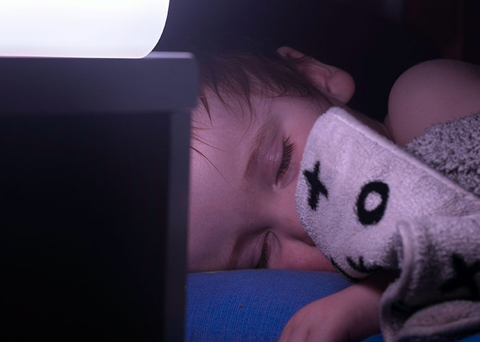 Sleeping child wrapped in a blanket near a night lamp, highlighting concerns about how a roommate’s guest treats her kid. Sleeping child wrapped in a blanket near a night lamp, highlighting concerns about how a roommate’s guest treats her kid.