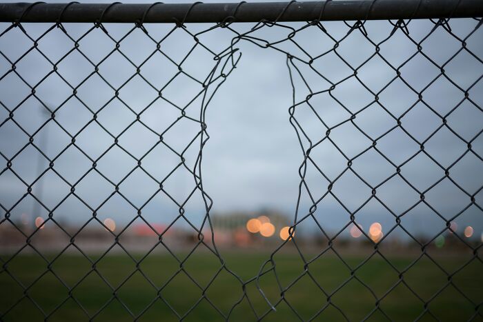 Chain-link fence with a large broken hole, symbolizing mind-boggling beliefs smart people still stand behind online.