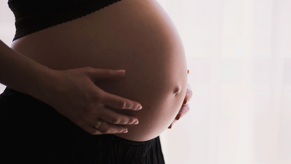 Close-up of a pregnant belly with hands gently cradling it, illustrating surprising things adults explain.