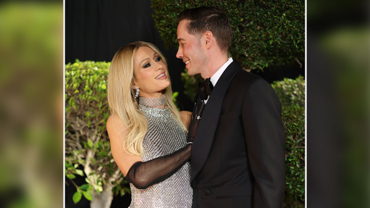 Carter Reum and a woman smiling at each other, dressed elegantly at an outdoor event with greenery in the background