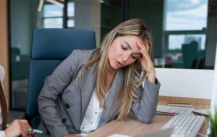 Stressed employee in business attire sitting at desk, showing frustration over boss obsessed with punctuality demands.