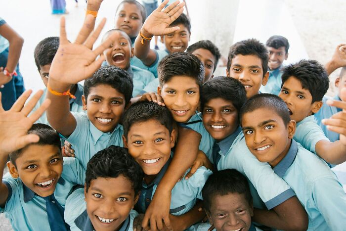 Group of smiling schoolboys in blue uniforms waving and posing happily, highlighting diverse beliefs smart people still hold online.