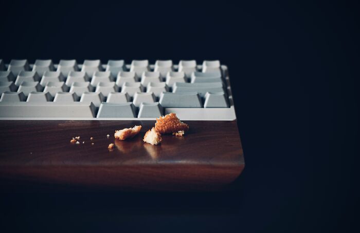Close-up of a keyboard with crumbs on a wooden desk, illustrating weird or disturbing things tech guys found fixing computers.