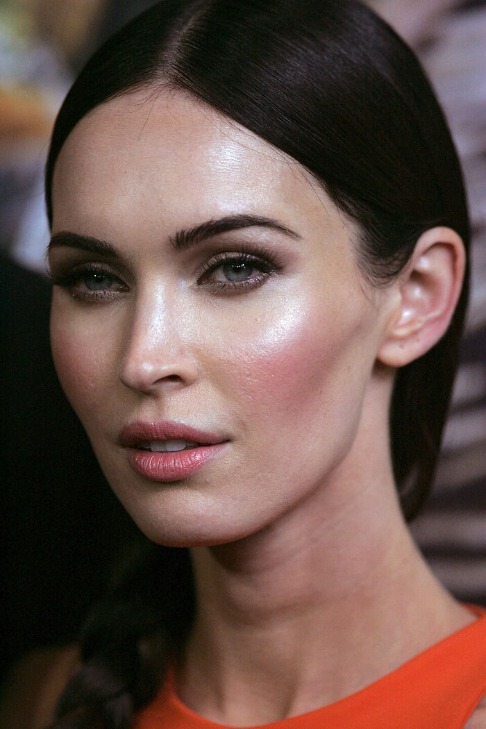 Close-up portrait of a woman with sleek dark hair and natural makeup discussing celebrity gossip and tea.