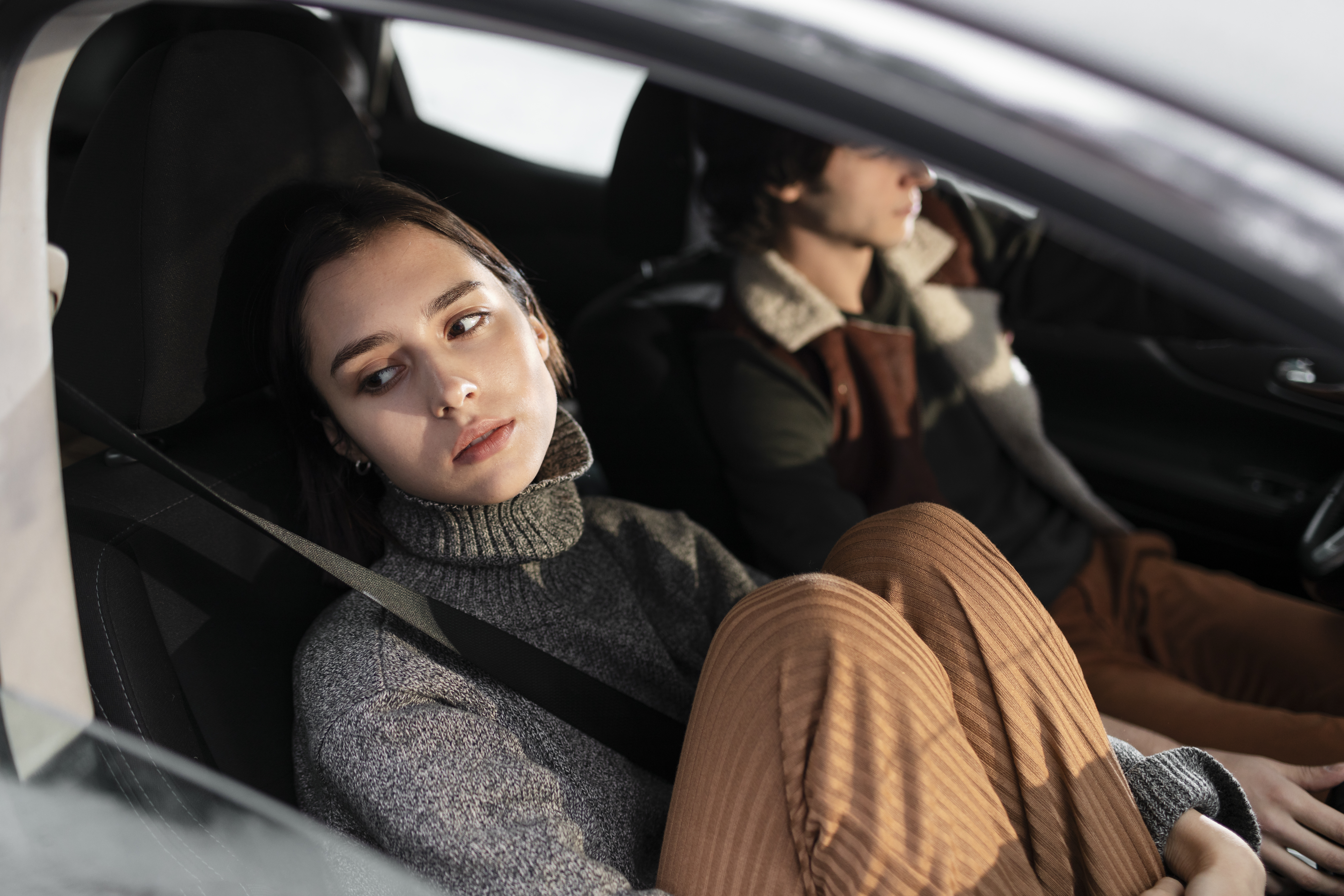 Woman looking away unhappily while sitting in a car with husband's childhood best friend driving the vehicle. Woman looking away unhappily while sitting in a car with husband's childhood best friend driving the vehicle.