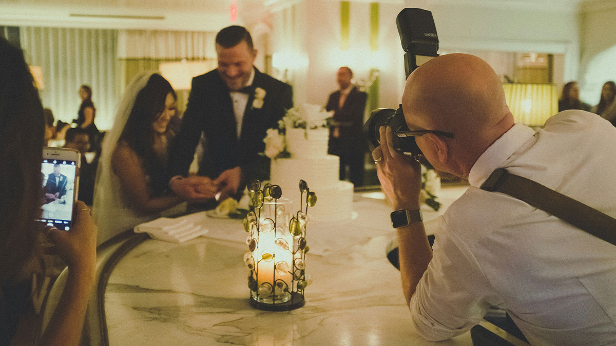 Wedding photographer taking pictures of couple cutting cake, cousin offers to photograph wedding as a gift.