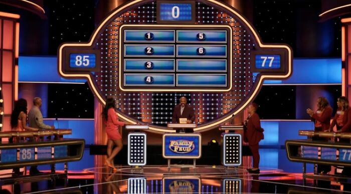 Contestants on Family Feud standing at podiums during a game round with host reading questions from cards. Contestants on Family Feud standing at podiums during a game round with host reading questions from cards.