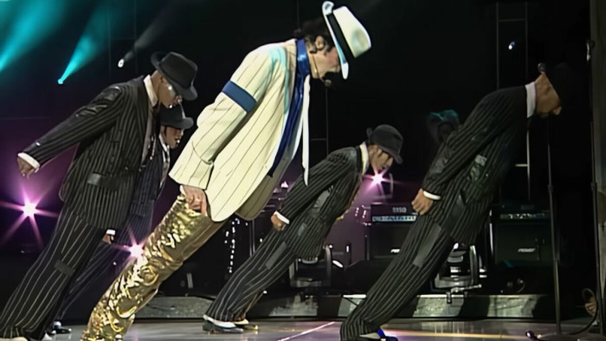 Michael Jackson performing his iconic lean on stage with dancers in pinstripe suits during a live concert.