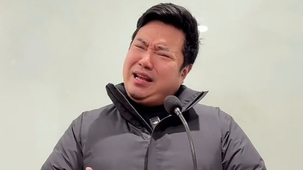 Chinese TikToker performing a viral impression of U.S. President with expressive facial gestures and a microphone.