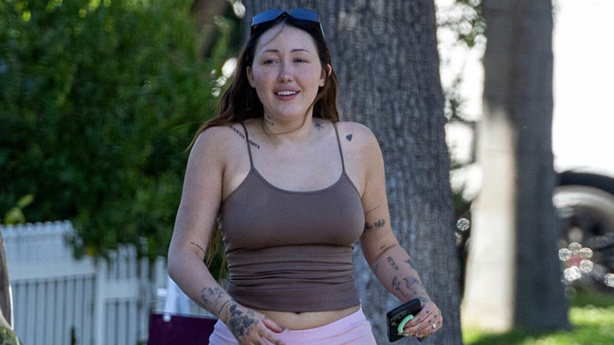 Noah Cyrus wearing a revealing top outdoors, displaying tattoos and holding a phone in a casual setting.