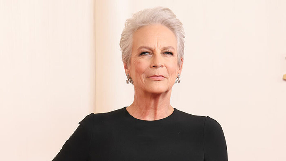 Jamie Lee Curtis posing confidently in a black dress, recalling plastic surgery prompted by an embarrassing cameraman remark.