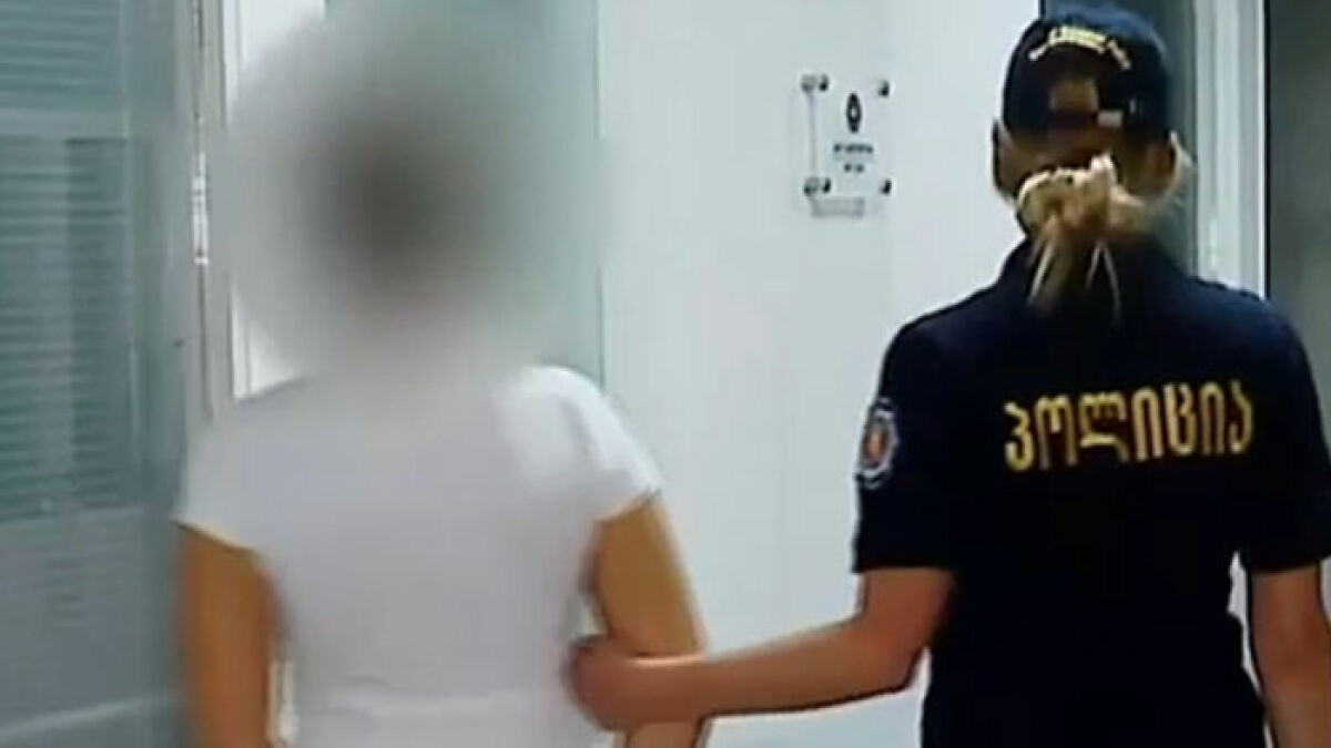 Teen who went missing in Thailand escorted by police officer in uniform inside a building hallway.