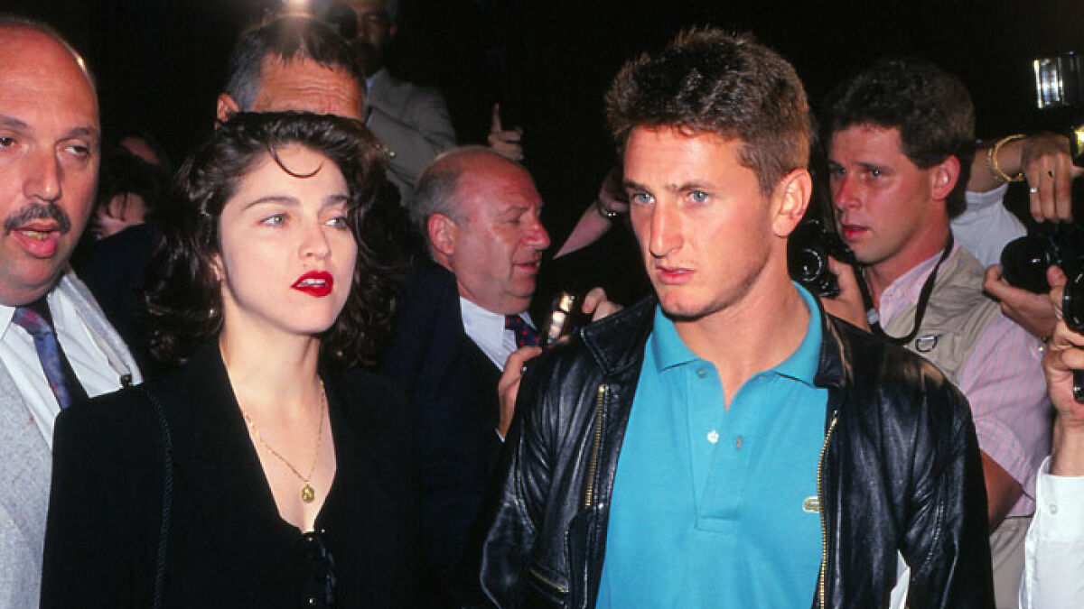 Sean Penn and Madonna walking at a public event surrounded by photographers and security personnel.