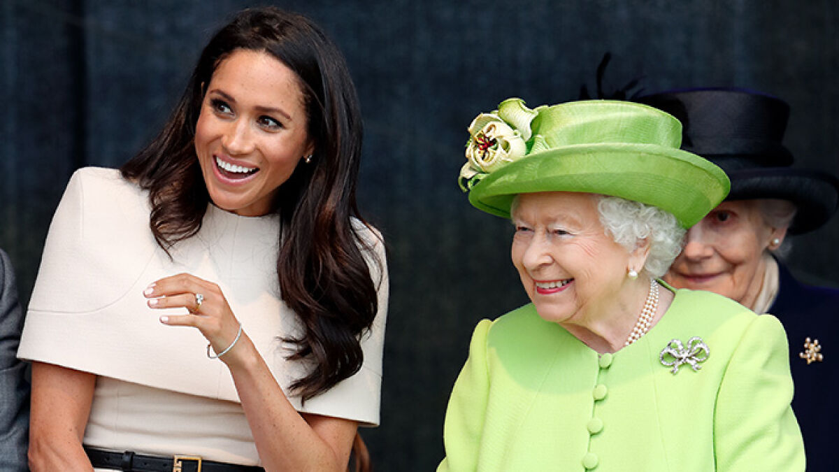 Meghan Markle smiling beside Queen Elizabeth, both engaged in conversation at a formal public event.