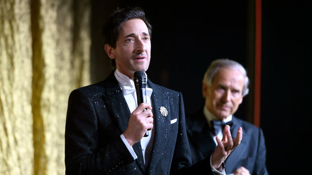 Adrien Brody speaking at an event, dressed formally, amid reactions to his art piece at Cannes.