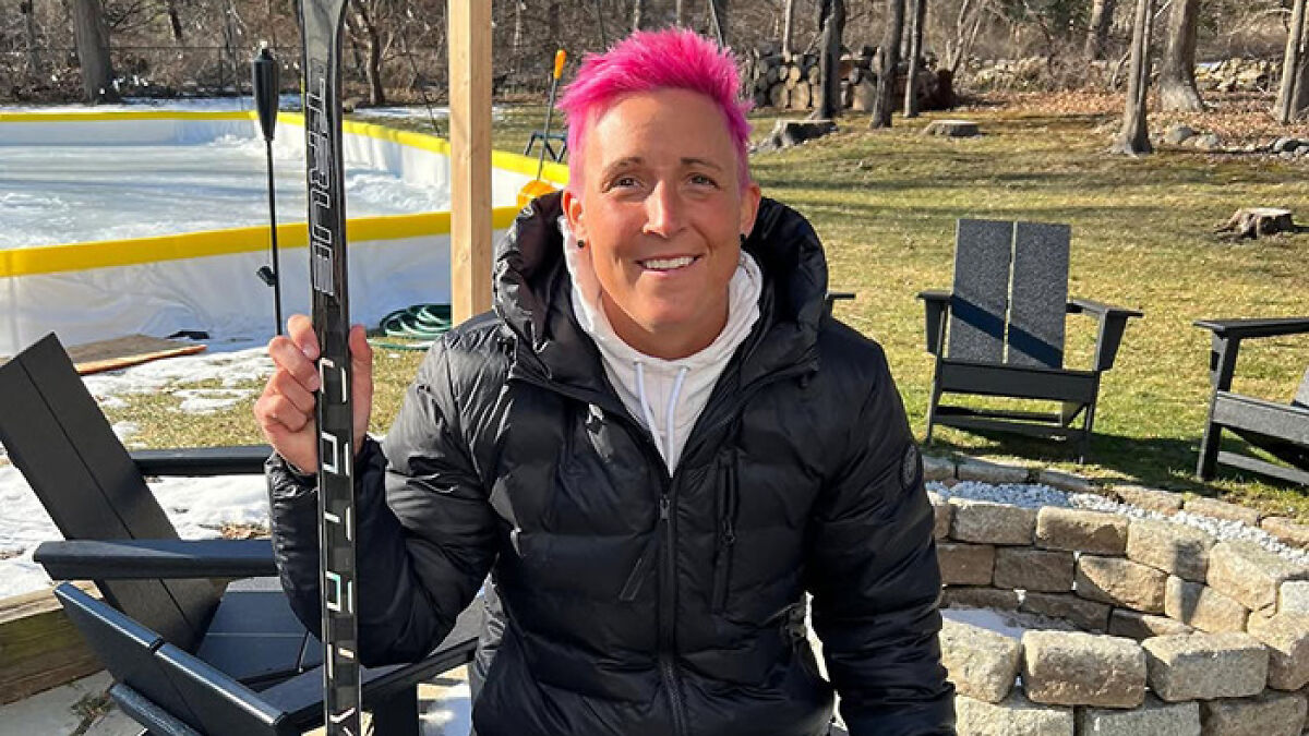 Female athlete with pink hair holding hockey stick outdoors near rink, highlighting restroom incident with female attendant.