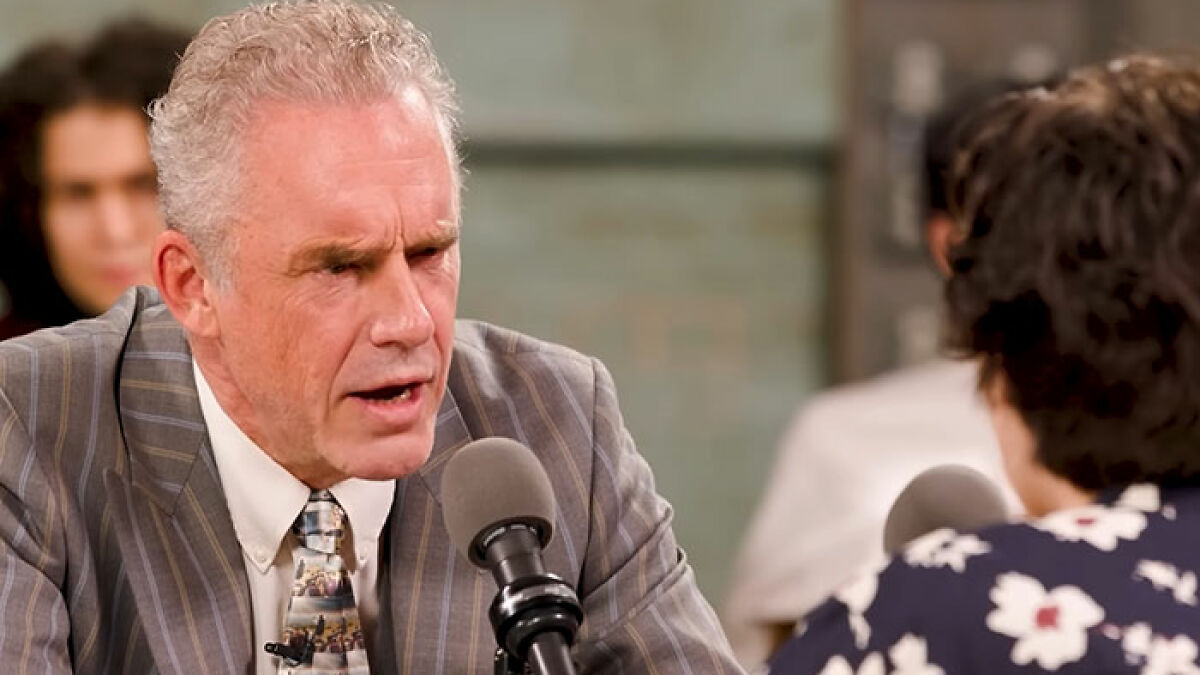 Jordan Peterson speaking intensely during a debate, facing opponents with microphones in an indoor setting.