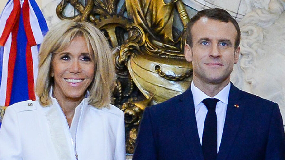 French President Emmanuel Macron and wife posing formally with a backdrop of ornate decorations and flags.