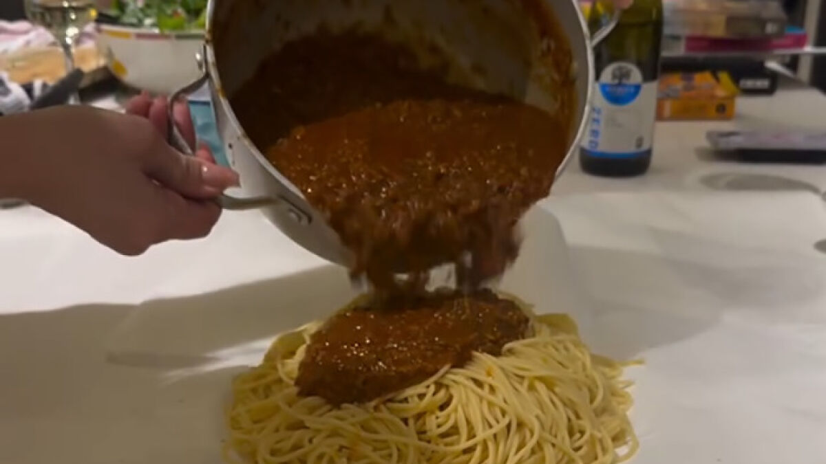 Hand pouring pasta sauce directly onto a mound of spaghetti served on a table without plates, parenting hack controversy.