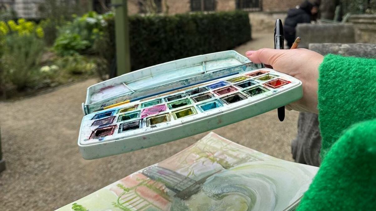 Watercolor palette and brush held by artist painting in the garden of Rubensu2019 house in Antwerp outdoors.
