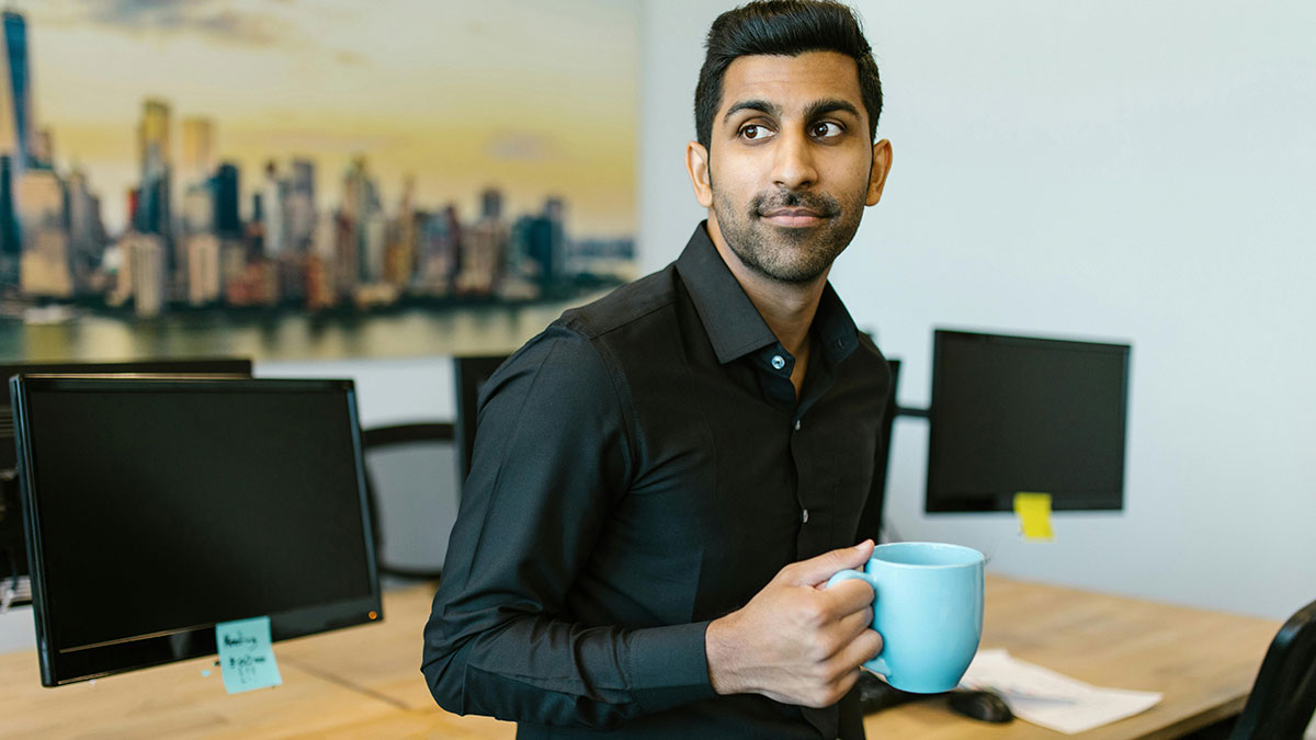 Man holding a mug in an office, looking sideways with a subtle expression, hinting at coworker mug stealing and coffee prank.