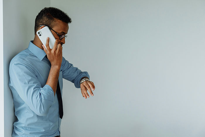 Young man in business attire looks at watch while talking on phone, illustrating helicopter mom calling son's boss. Young man in business attire looks at watch while talking on phone, illustrating helicopter mom calling son's boss.