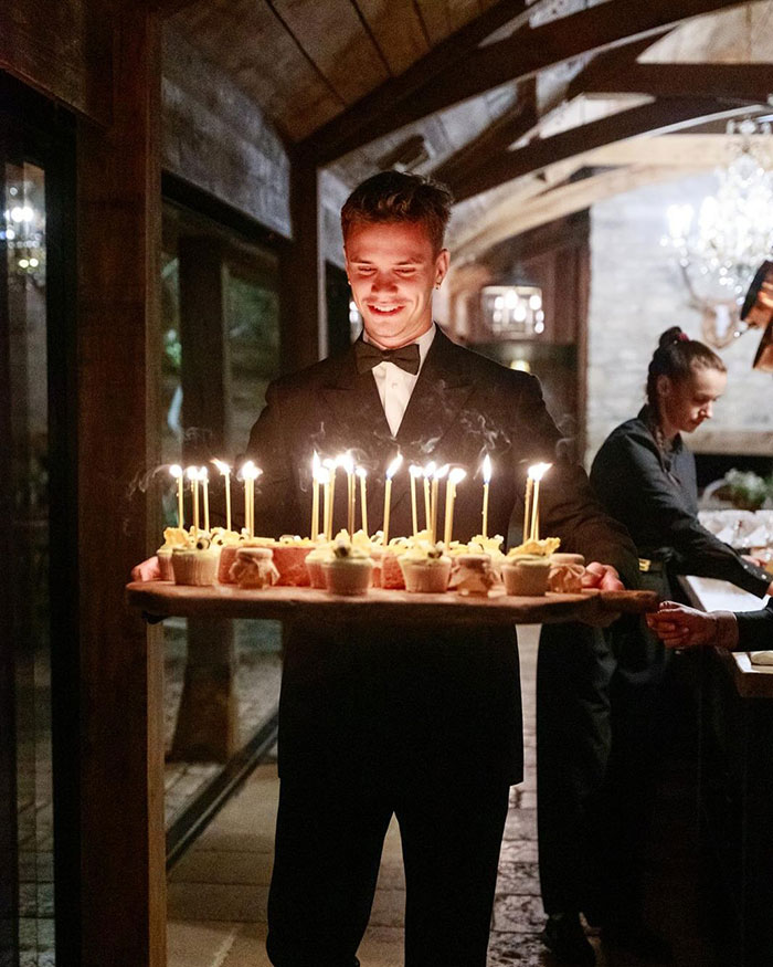 Young man in tuxedo holding birthday cupcakes with lit candles at David Beckham 50th birthday party family event. Young man in tuxedo holding birthday cupcakes with lit candles at David Beckham 50th birthday party family event.