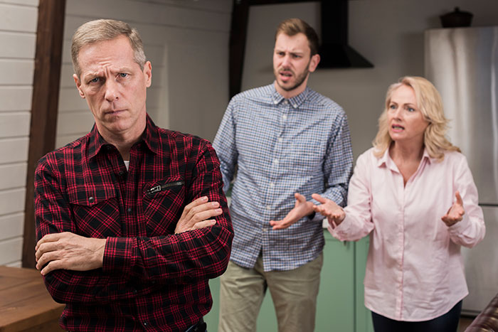 Man prioritizing his miniature wargaming studio, standing arms crossed while daughter and fiancé argue in the background. Man prioritizing his miniature wargaming studio, standing arms crossed while daughter and fiancé argue in the background.