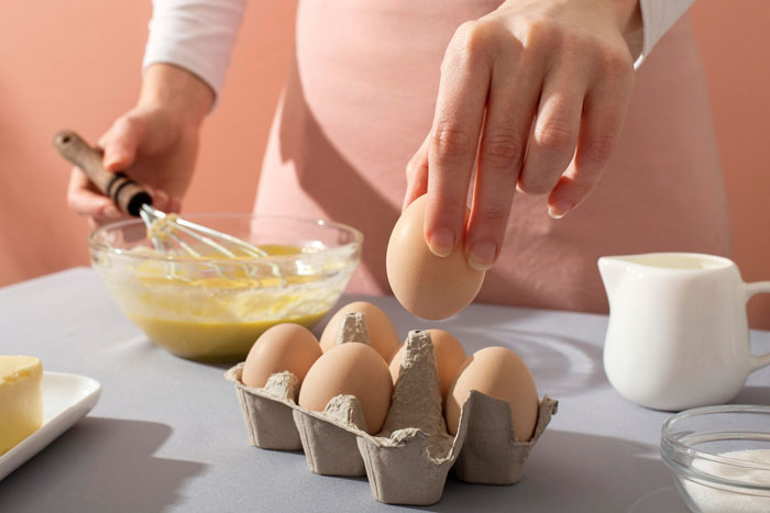 Hand holding an egg over carton with eggs beside a bowl of batter, illustrating eggs are dairy confusion in baking. Hand holding an egg over carton with eggs beside a bowl of batter, illustrating eggs are dairy confusion in baking.