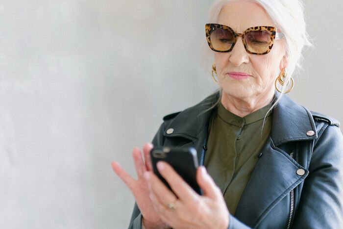 Older woman in sunglasses and leather jacket looking at her phone, reflecting family trip conflict about boyfriends not counting. Older woman in sunglasses and leather jacket looking at her phone, reflecting family trip conflict about boyfriends not counting.